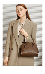 Woman holding a brown handbag wearing a beige coat against a neutral background