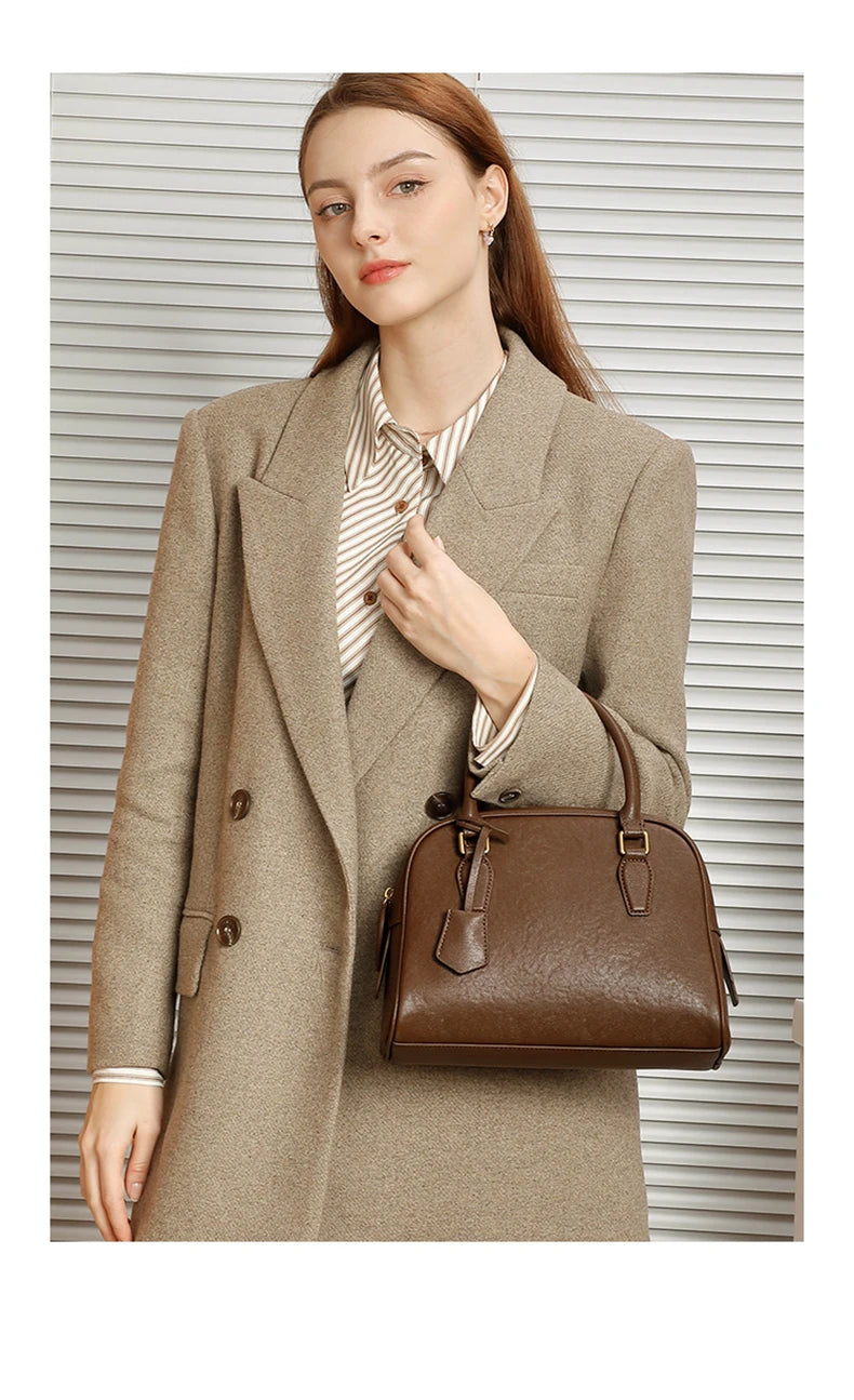 Woman holding a brown handbag wearing a beige coat against a neutral background