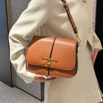 Person holding a brown leather handbag with gold accents
