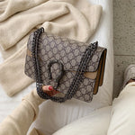 Patterned handbag with chain detail held by a person sitting on a couch.