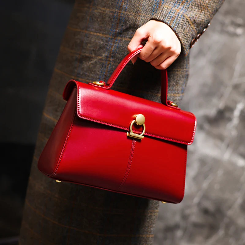 Red handbag held by a person wearing a patterned coat.