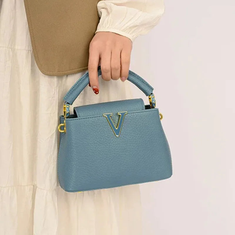 Blue handbag with gold accents held by a person against a neutral background