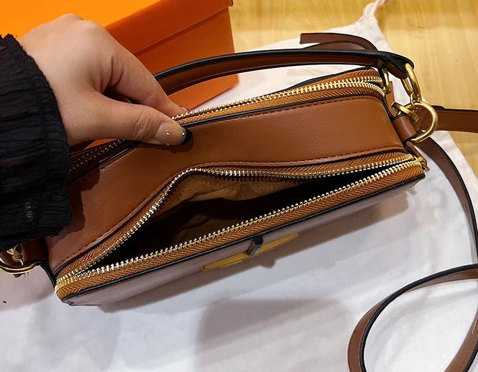 Brown handbag with gold zipper being held open, orange box in the background