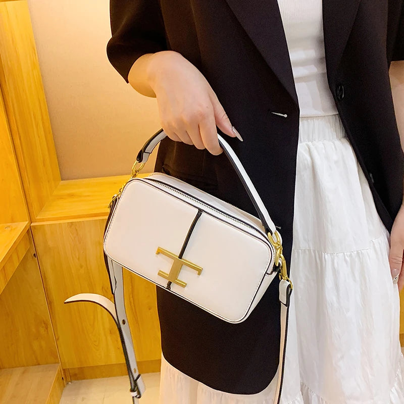 Person holding a white handbag with a gold logo in front of a wooden wall.