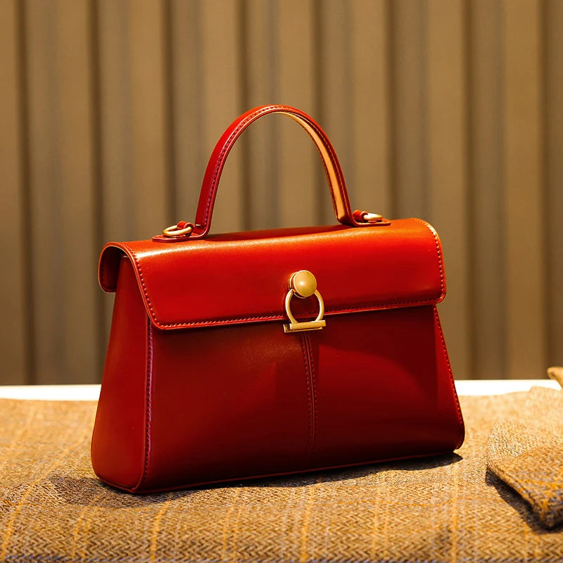 Red handbag with a gold clasp on a textured surface with a neutral background