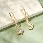 Gold earrings with gemstones on a light green surface