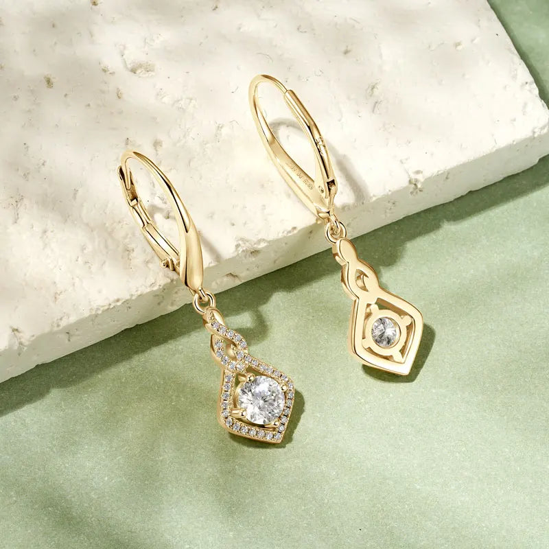 Gold earrings with gemstones on a light green surface
