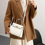 Person wearing a brown blazer holding a white handbag with a gold clasp.