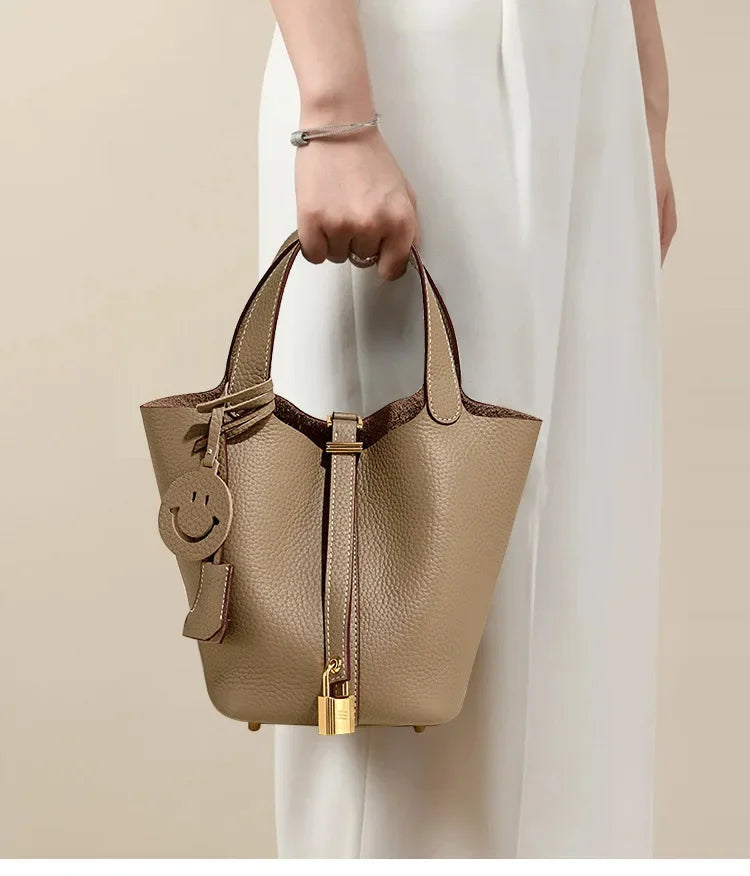 Beige handbag with smiley face keychain held by a person wearing a white dress.