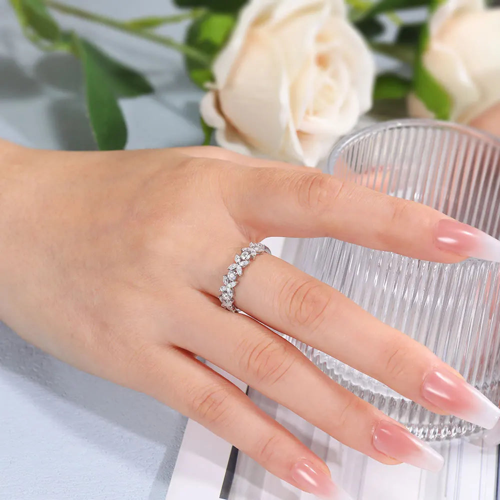 Hand wearing a silver ring with pink nail polish against a blurred floral background
