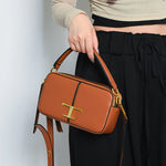 Brown handbag with gold 'T' logo held by a person wearing black pants and a beige top.