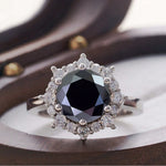 Ring with a central black gemstone and diamond-studded halo on a wooden surface