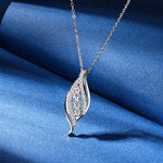 Silver necklace with a leaf-shaped pendant on a blue fabric background