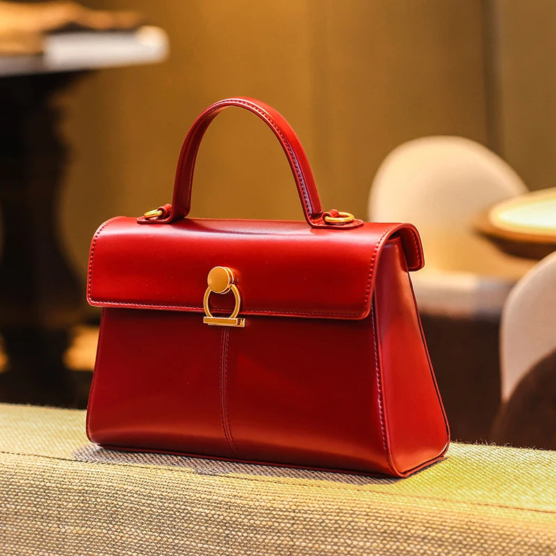 Red handbag with gold accents on a textured surface with blurred background