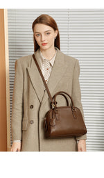 Woman in a beige coat holding a brown handbag against a neutral background