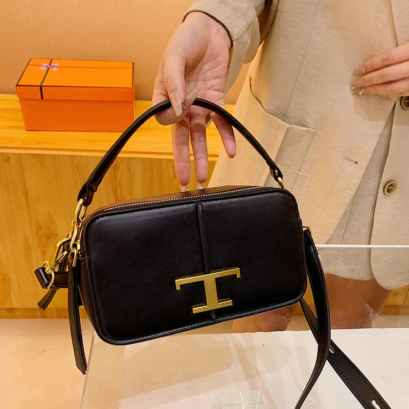 Black handbag with gold logo held by a person, with an orange box in the background.