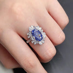 Ring with a blue gemstone and diamond accents on a finger against a neutral background
