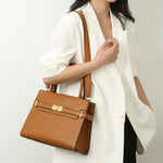 Brown handbag held by a person wearing a white blazer on a light gray background