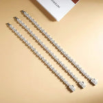 Two diamond necklaces on a beige surface with a magazine in the background