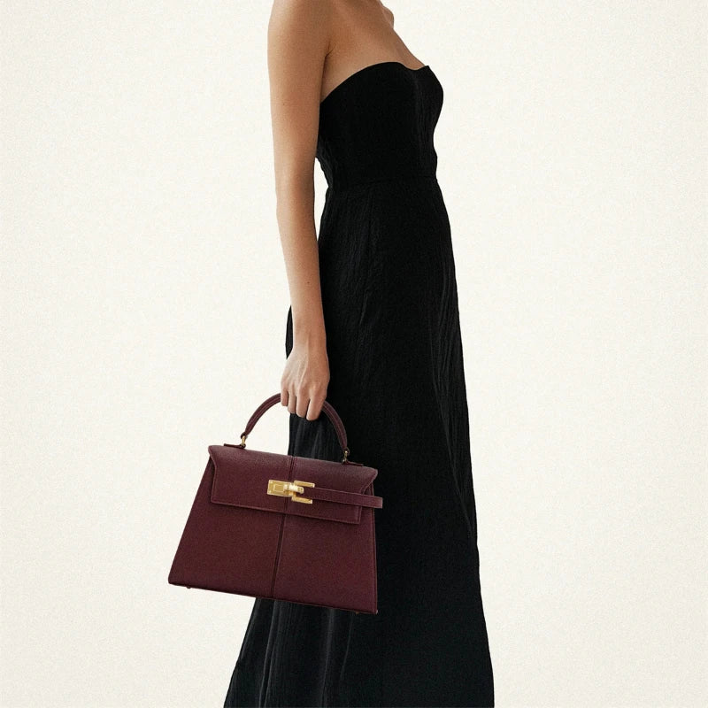 Woman holding a burgundy handbag with a gold clasp against a white background