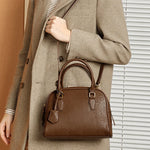 Person wearing a beige coat holding a brown handbag indoors.