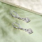 Silver earrings with gemstones on a light green fabric background