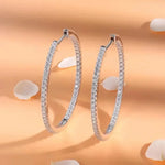 Pair of silver hoop earrings with clear gemstones on a peach background with white petals.