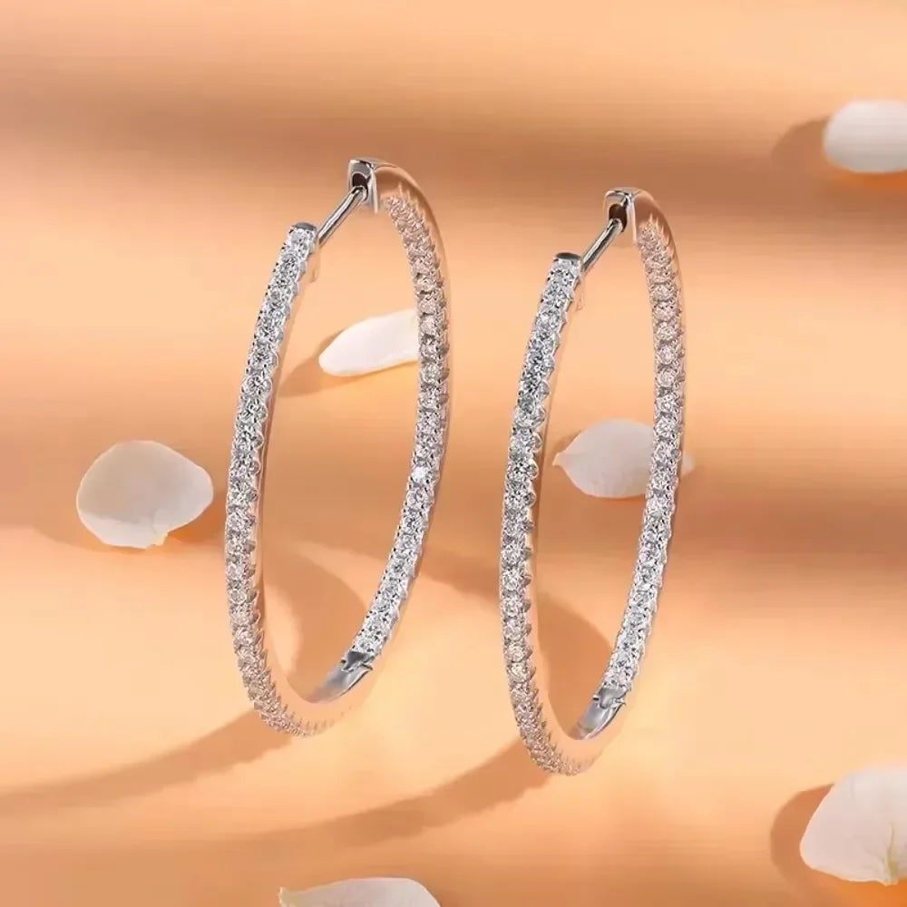 Pair of silver hoop earrings with clear gemstones on a peach background with white petals.