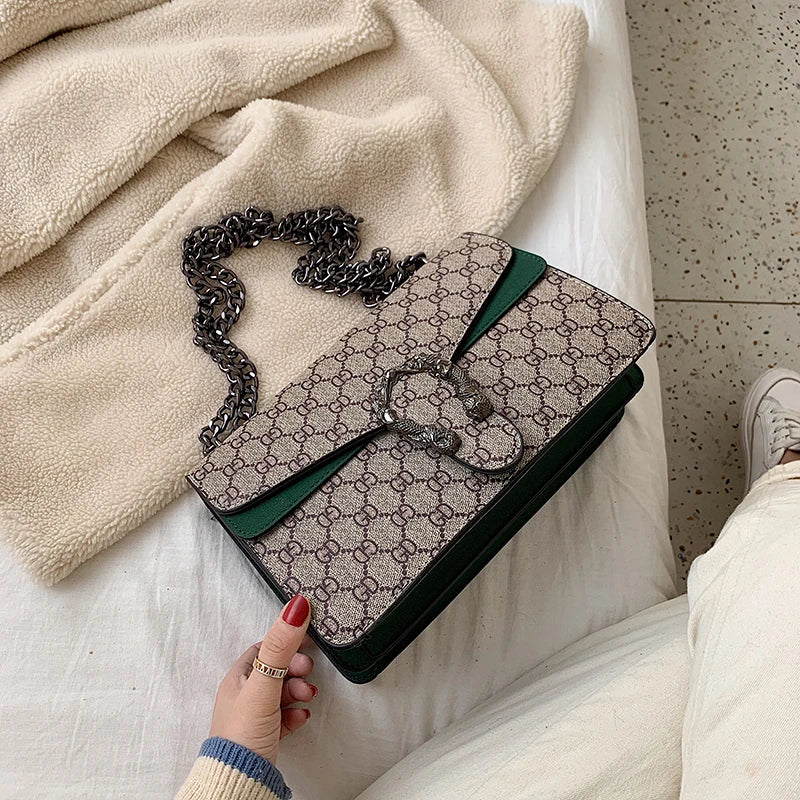 Patterned handbag with chain strap held by a hand on a soft surface.