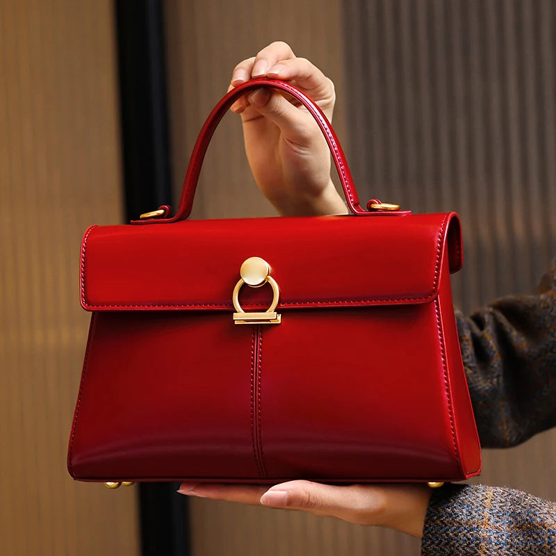 Red handbag with gold accents held by a person against a neutral background