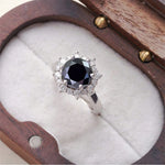 Ring with a black gemstone and diamond accents in a wooden box