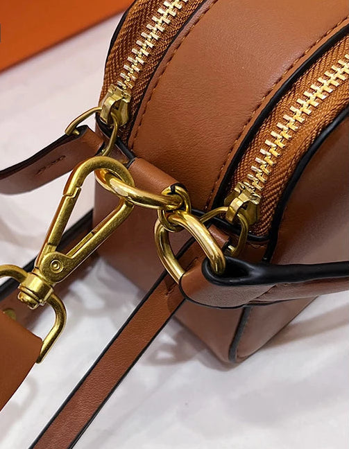 Brown leather handbag with gold zipper and clasp on a white background