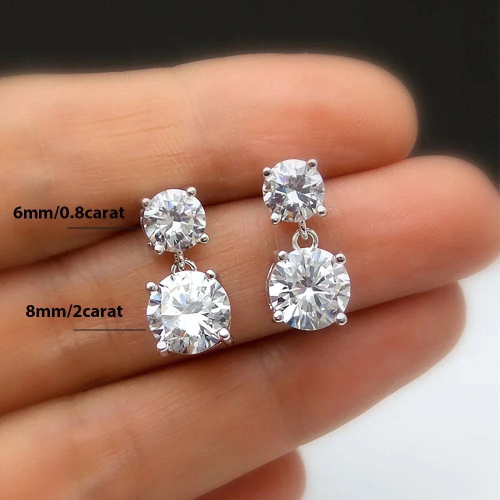 Diamond earrings held between fingers with size labels on a blurred background
