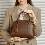 Person holding a brown handbag against a neutral background