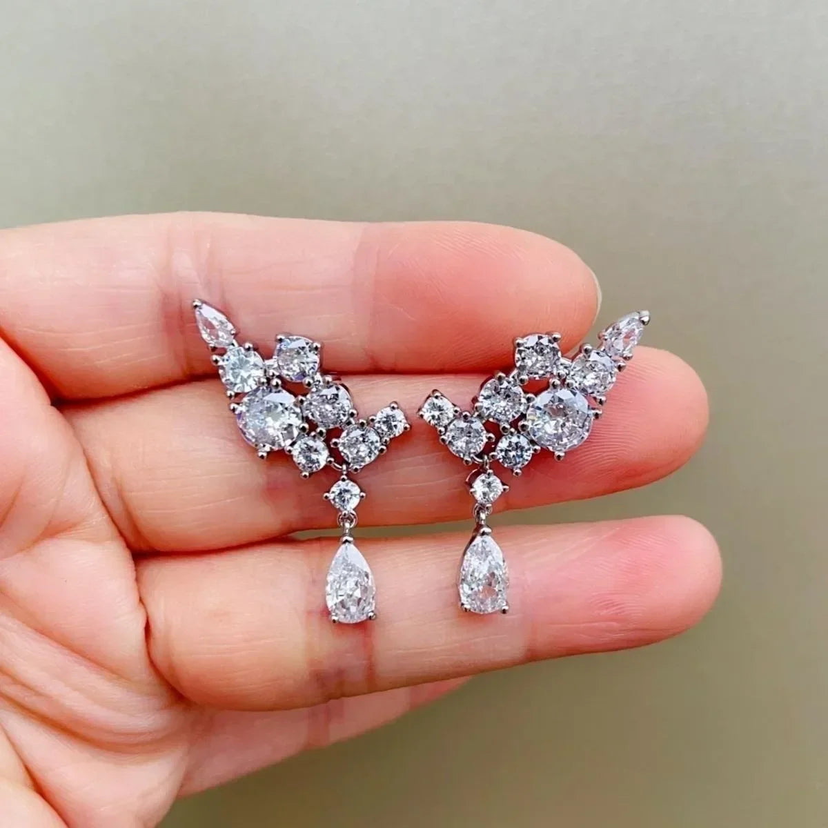 Pair of diamond earrings held between fingers against a neutral background