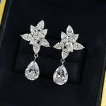 Pair of silver earrings with floral and teardrop designs on a black background