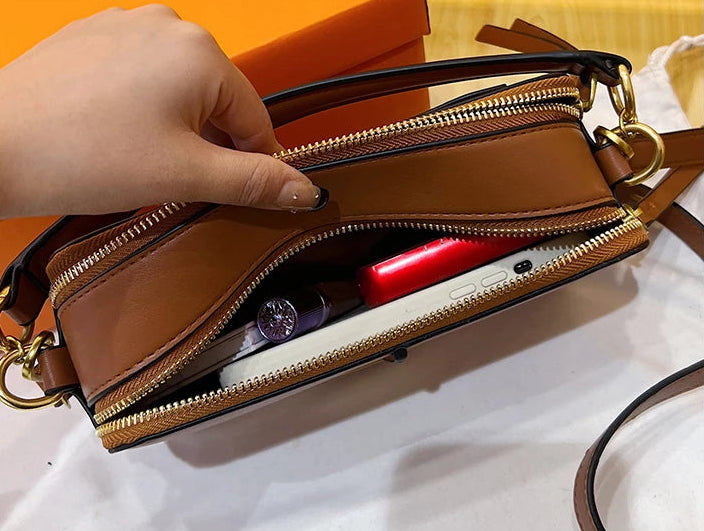 Brown handbag with gold zippers held by a hand, with an orange box in the background.