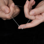 Silver necklace with a V-shaped pendant held between two hands against a black background