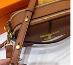 Brown leather handbag with gold hardware on a white surface with an orange background