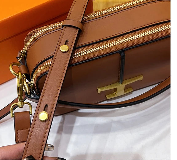Brown leather handbag with gold hardware on a white surface with an orange background