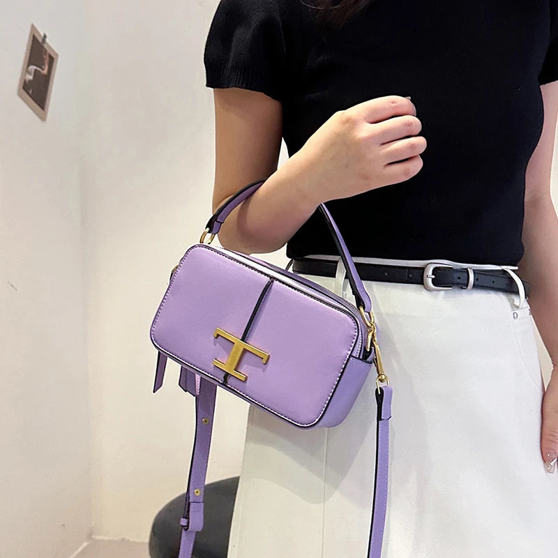 Person holding a purple handbag with a gold clasp against a neutral background