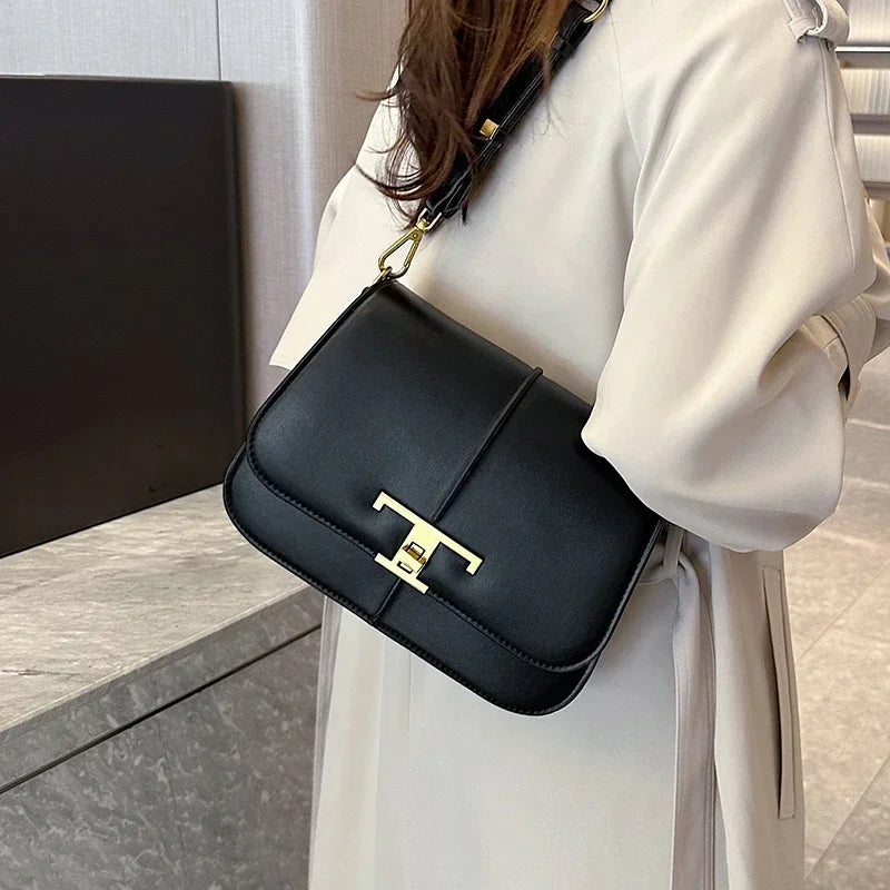Black handbag with gold clasp worn by a person in a white coat.