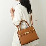 Brown handbag held by a person wearing a white outfit on a light gray background