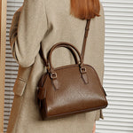 Brown handbag held by a person wearing a beige coat against a neutral background