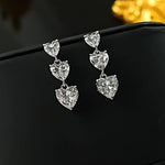 Heart-shaped silver earrings on a black surface with a blurred gold object in the background