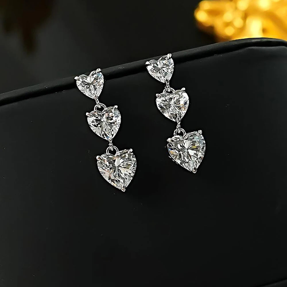 Heart-shaped silver earrings on a black surface with a blurred gold object in the background