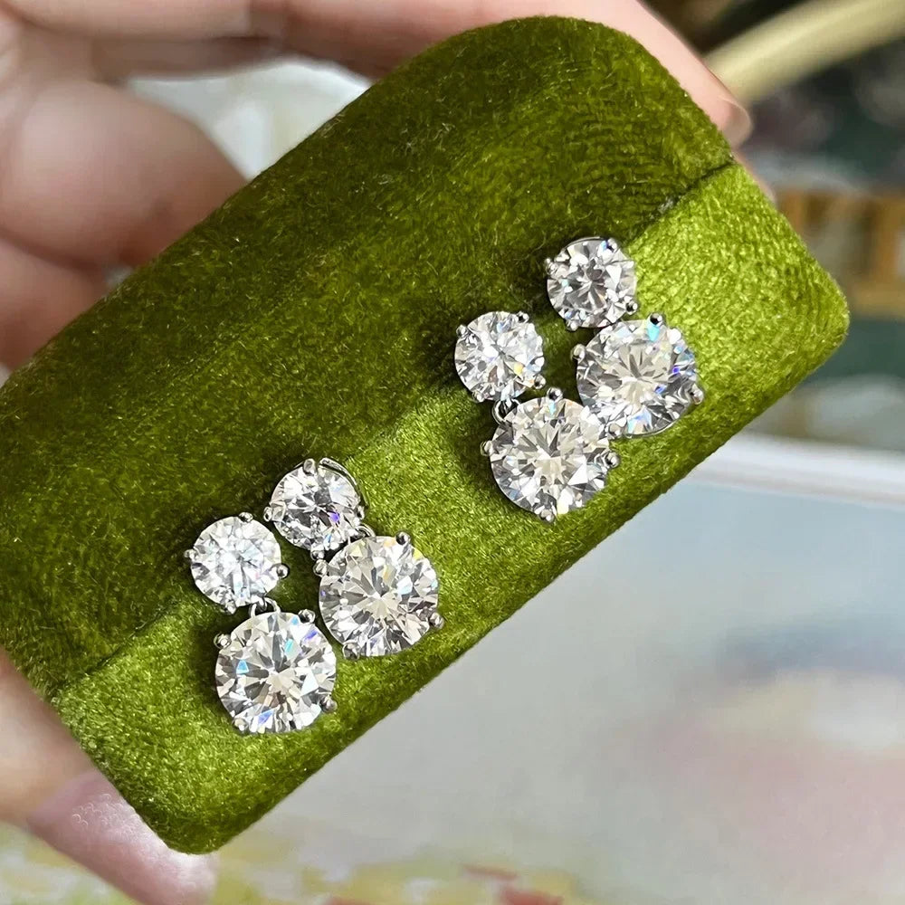 Pair of diamond earrings on a green cushion held by a hand.