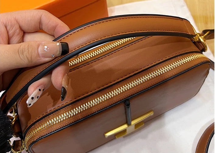 Brown handbag with gold zipper and hardware, held by a hand against an orange box background.