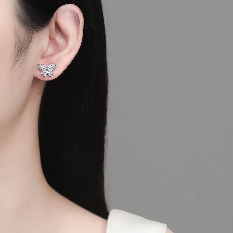 Close-up of a person wearing a butterfly-shaped earring against a neutral background