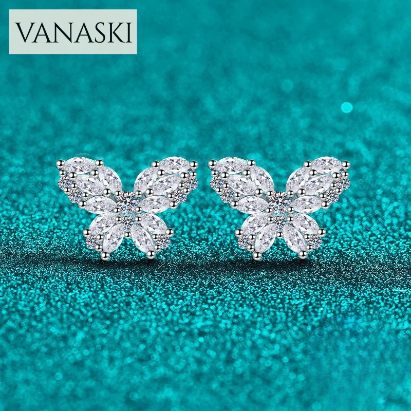 Butterfly-shaped earrings with clear stones on a turquoise glittery background, featuring the Vanaski brand.